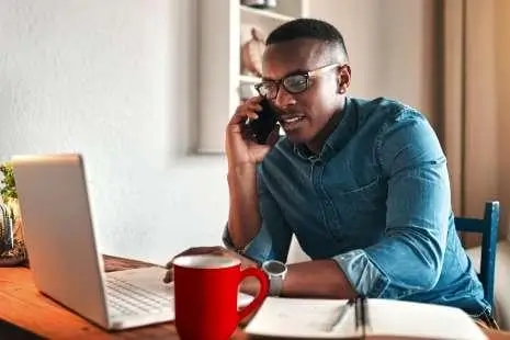 man talking on phone while looking at laptop