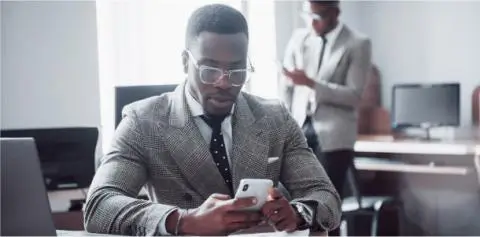 man sitting at desk in front of his laptop using his phone in the office