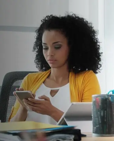 women looking at her phone with a tablet on her desk