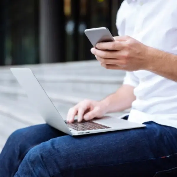 male sitting with laptop on lap and ohone in his hand