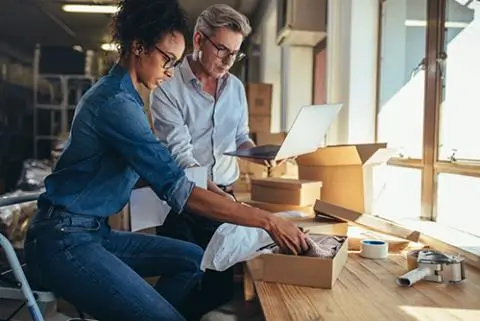 woman looking at something in a box while a gentelman is looking at his laptop