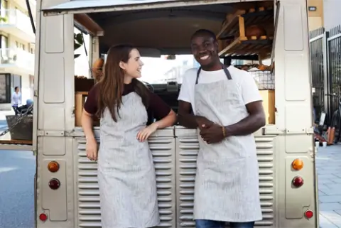 man and woman in aprons leaning against a food truck