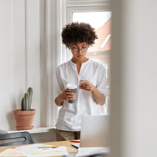 A women holding a coffee cup and looking at her phone