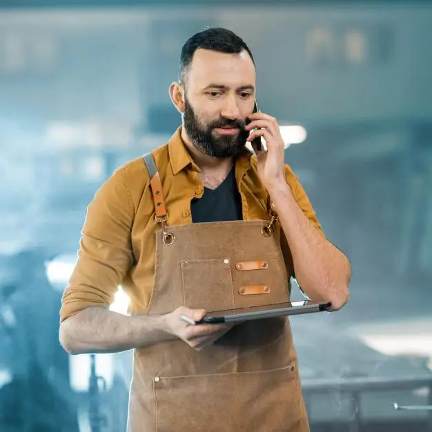 man in apron talking on his phone while holding a tablet
