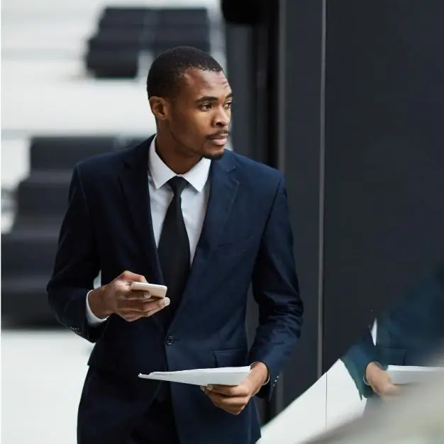 Man in a suit walking with a phone in his one hanf and a document in the other hand