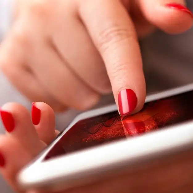a women's hand wearning red nailpolish using a phone