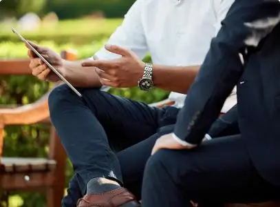 two men sitting on a bench outside looking at a tablet