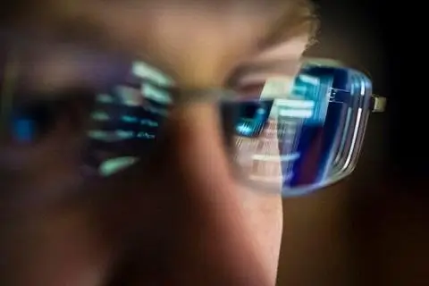 mans fance with glasses reflecting his laptop screen