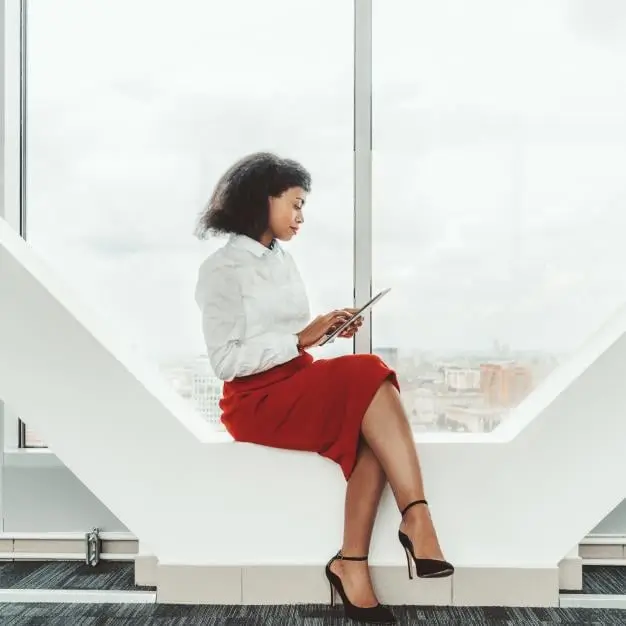 A woman sitting at window working from her tablet