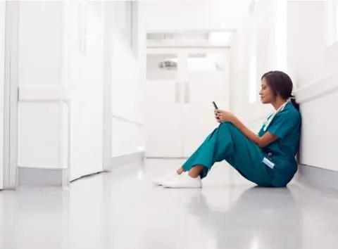 Nurse sitting on floor in hospital floor looking at her phone