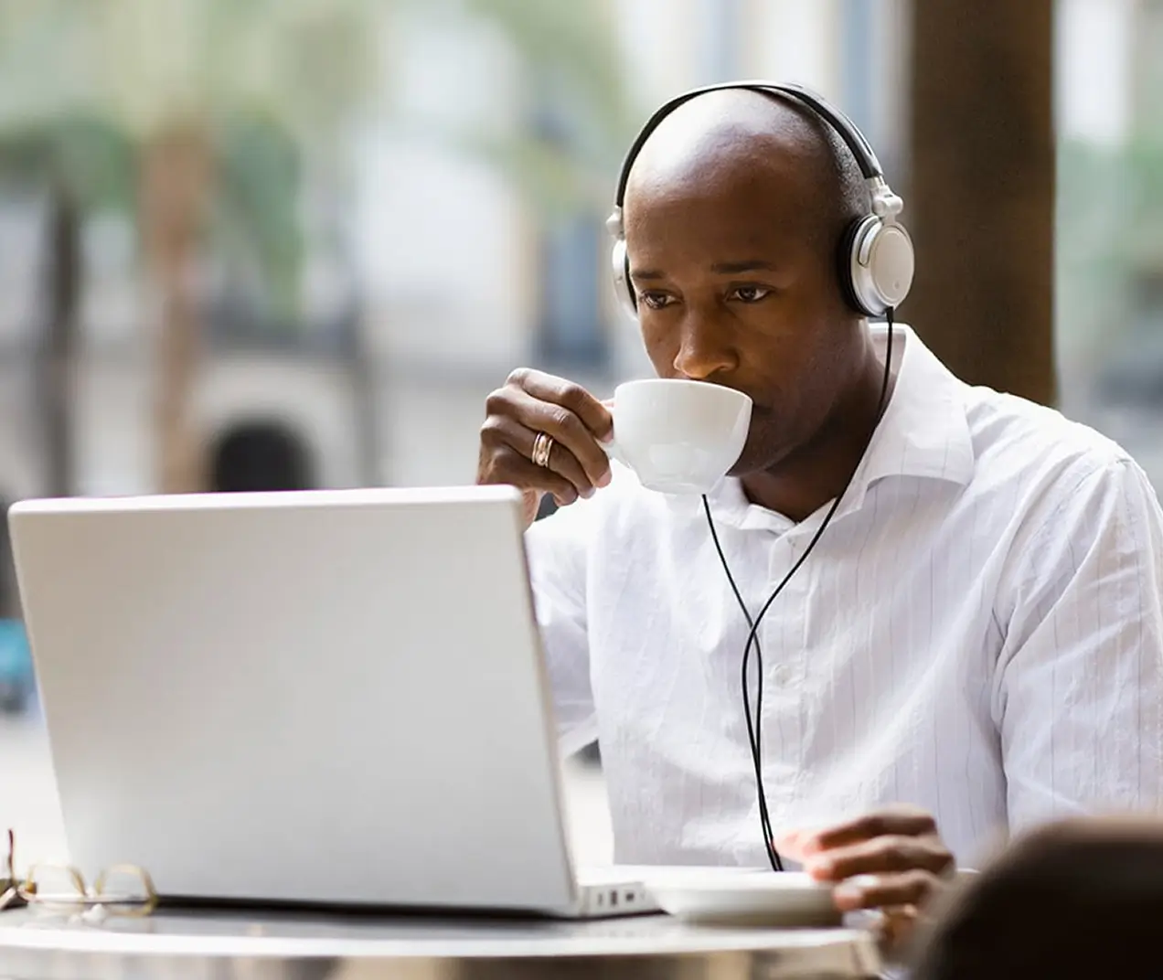 Man wearing headphones drinking coffee while working on a laptop 