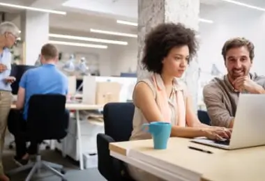 Colleagues collaborating and looking at a laptop computer together in an open-plan office