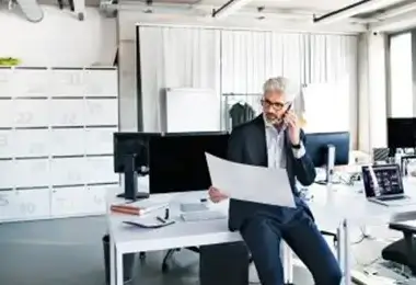 Businessman reviewing documents while talking on the phone at his office desk