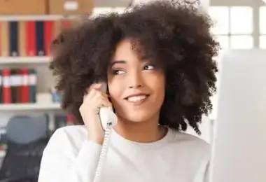 Smiling woman talking on a landline telephone at her desk