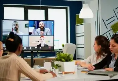 Team of colleagues participating in a video conference meeting on a large screen in the office