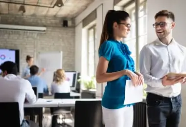 Colleagues discussing work while holding documents in a busy modern office